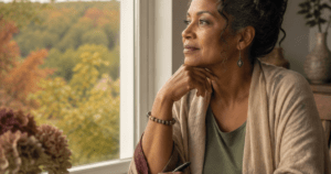 Frau blickt beim Schreiben in ihr Journal ruhig aus einem herbstlichen Fenster.