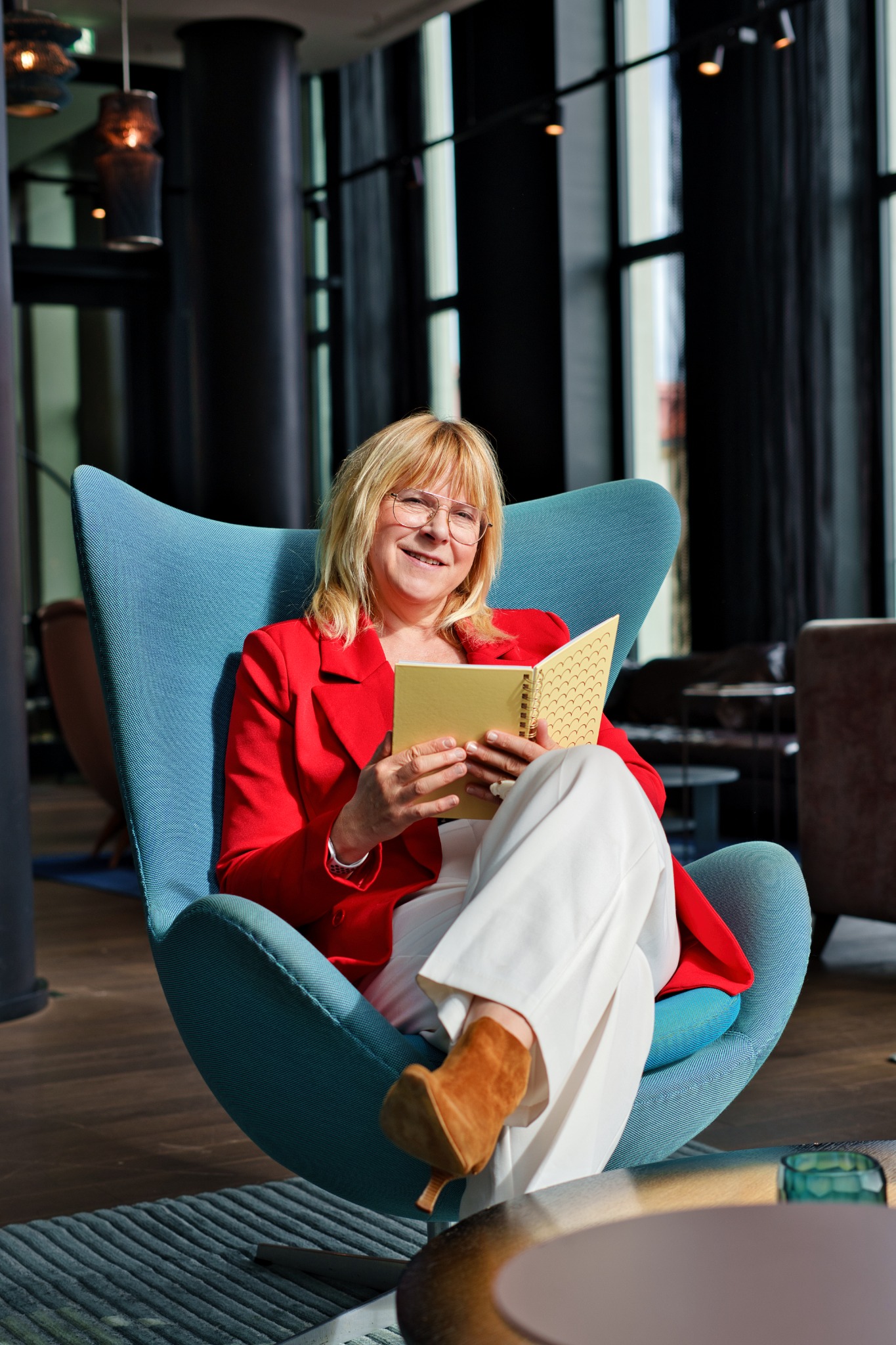 Sabine Blumhoff sitzt mit einem Notizbuch im blauen Sessel.
